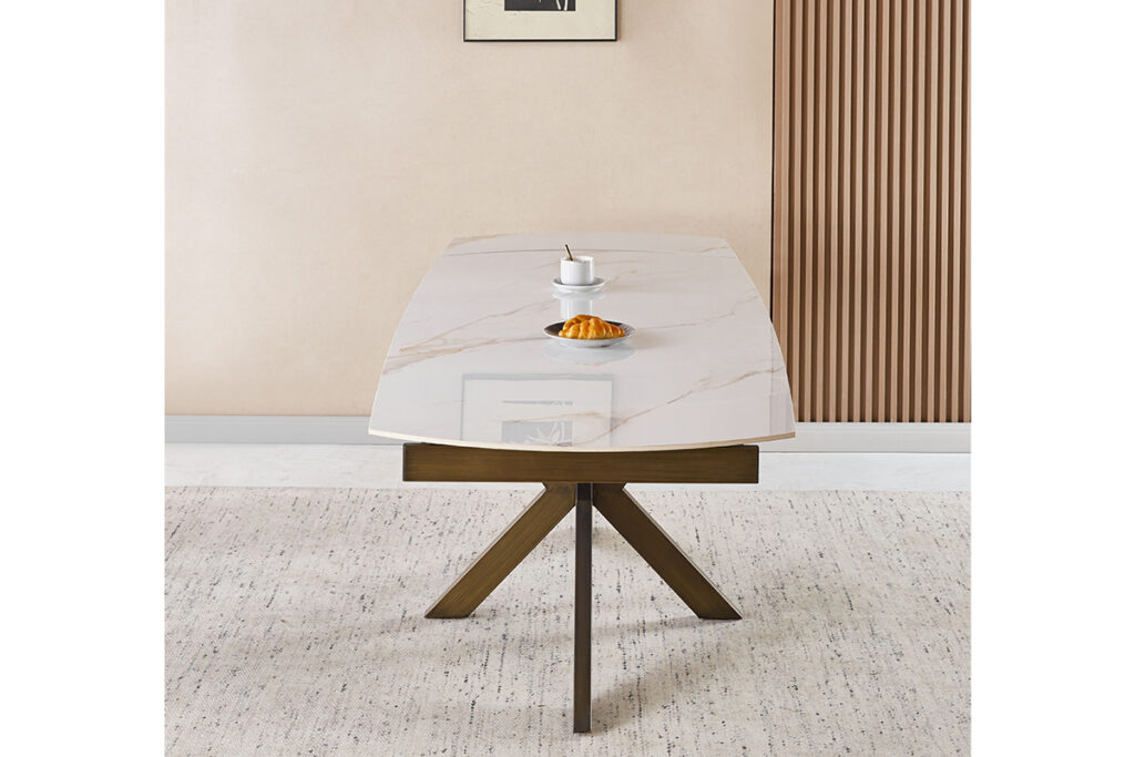 Modern marble-top dining table with wooden X-frame legs in a beige room, topped with a cup and saucer and a croissant on a small plate.